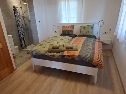 Schlafzimmer mit Doppelbett im weißen Rahmen und offenem Badbereich